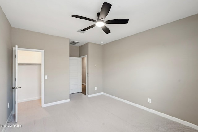 unfurnished bedroom with ceiling fan, a spacious closet, a closet, and light carpet