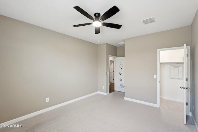 unfurnished bedroom featuring a walk in closet, light colored carpet, ceiling fan, and a closet