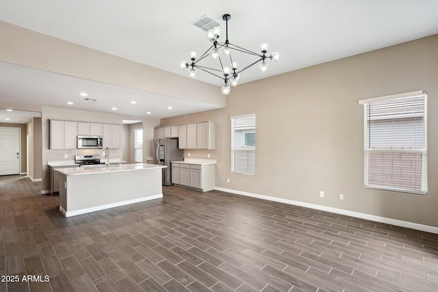 kitchen with appliances with stainless steel finishes, sink, hanging light fixtures, a notable chandelier, and a center island with sink