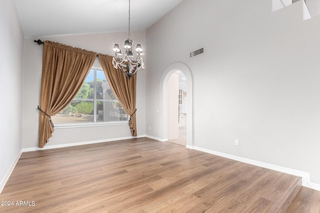 spare room featuring arched walkways, a chandelier, light wood finished floors, baseboards, and high vaulted ceiling