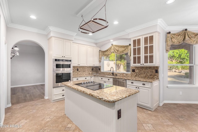 kitchen with appliances with stainless steel finishes, a sink, light stone countertops, a kitchen island, and backsplash