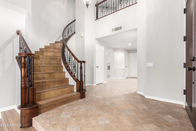 entryway with baseboards, a high ceiling, stone finish floors, and stairs