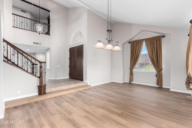 entrance foyer with stairs, baseboards, wood finished floors, high vaulted ceiling, and a chandelier
