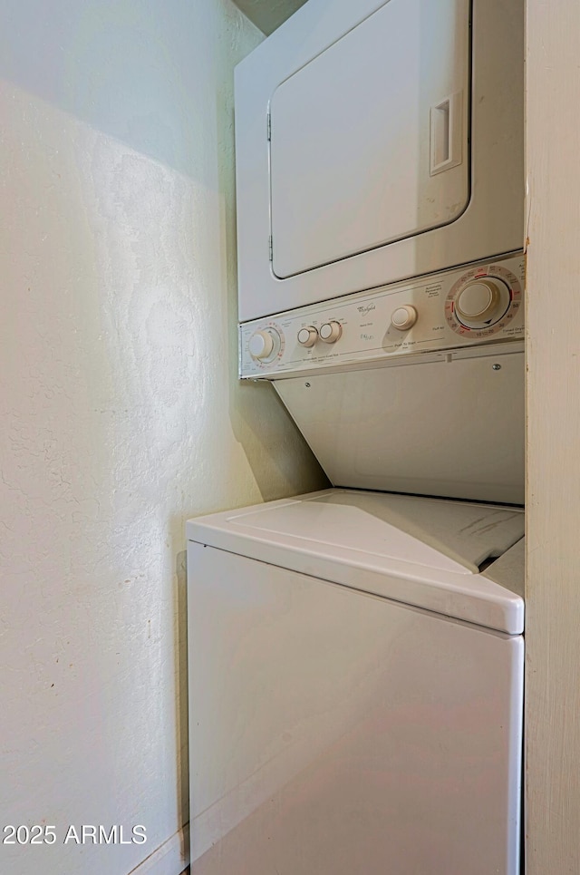 clothes washing area with laundry area, stacked washer / drying machine, and a textured wall