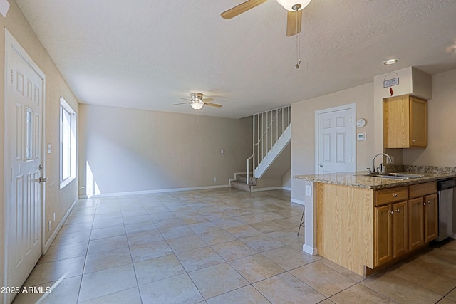 kitchen featuring baseboards, ceiling fan, a sink, stone counters, and stainless steel dishwasher