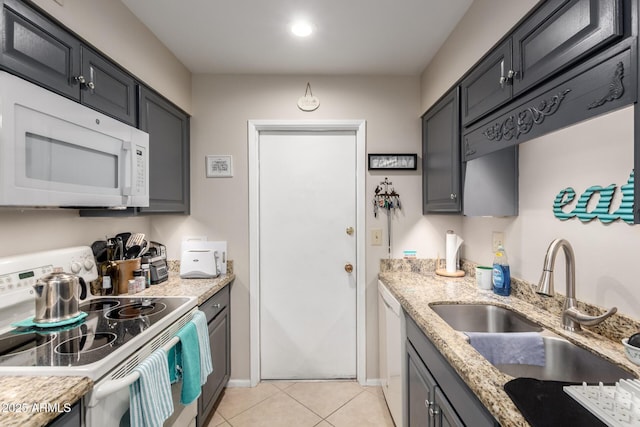 kitchen with light stone countertops, white appliances, a sink, and light tile patterned floors