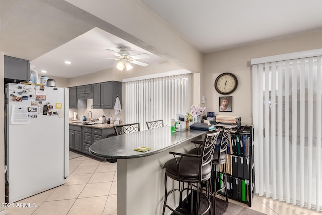 kitchen featuring light tile patterned floors, a breakfast bar area, freestanding refrigerator, gray cabinetry, and a sink