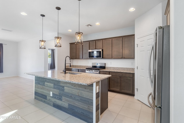 kitchen featuring hanging light fixtures, stainless steel appliances, a center island with sink, sink, and light stone counters