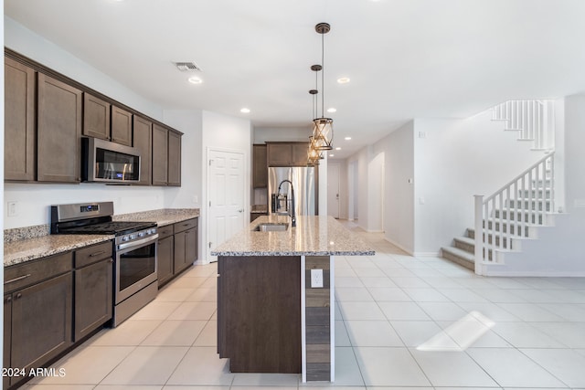 kitchen with dark brown cabinets, a center island with sink, appliances with stainless steel finishes, light stone countertops, and pendant lighting