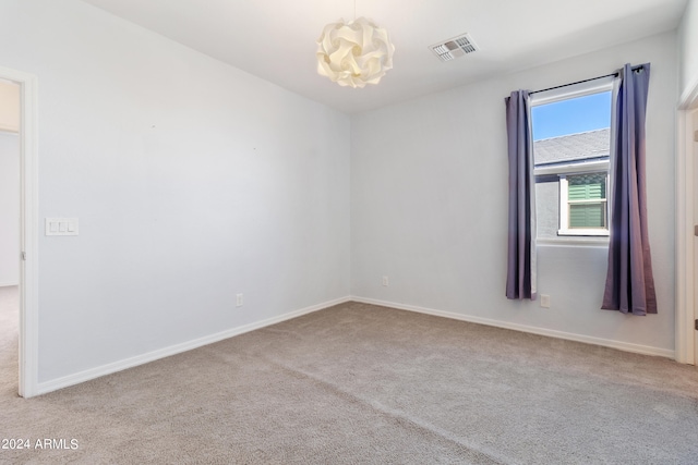 carpeted spare room featuring a chandelier