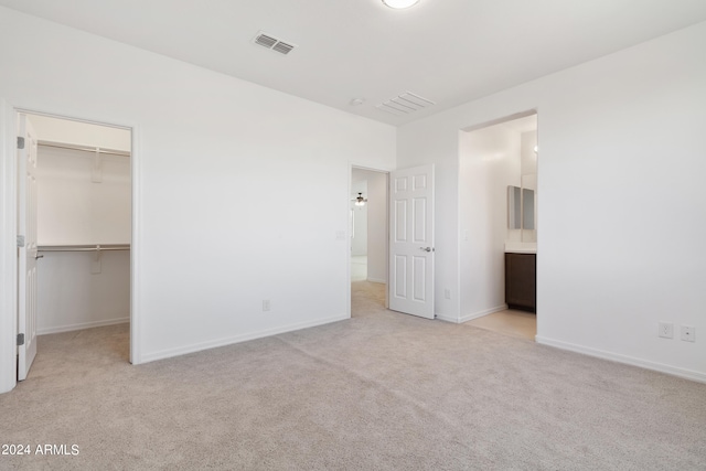 unfurnished bedroom featuring connected bathroom, light carpet, a walk in closet, and a closet