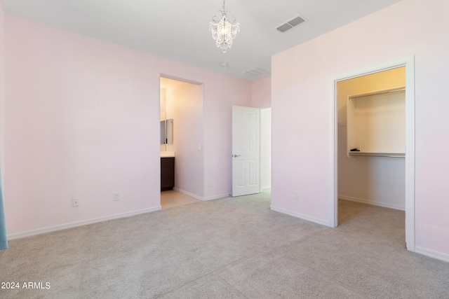 unfurnished bedroom featuring a closet, light carpet, a spacious closet, a notable chandelier, and ensuite bathroom