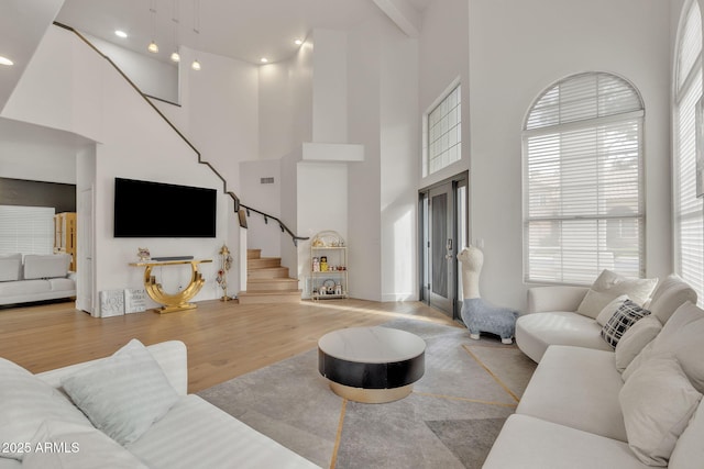 living area with french doors, light wood finished floors, visible vents, a towering ceiling, and stairway