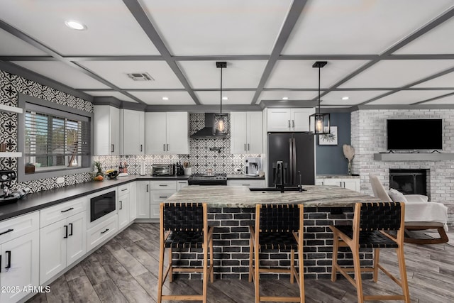 kitchen with visible vents, coffered ceiling, a sink, appliances with stainless steel finishes, and wall chimney range hood