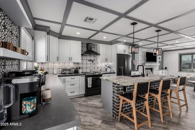 kitchen featuring visible vents, wall chimney range hood, refrigerator with ice dispenser, black range with gas cooktop, and a sink