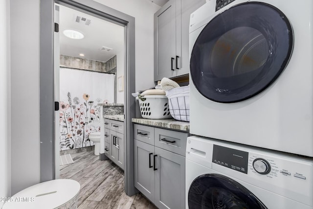 laundry room with stacked washer / dryer, cabinet space, light wood-type flooring, and visible vents