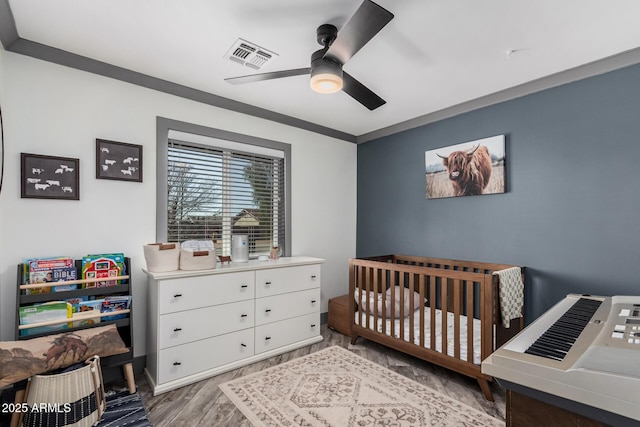 bedroom with ceiling fan, visible vents, a nursery area, and wood finished floors