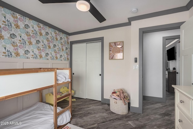 bedroom with a wainscoted wall, dark wood-style flooring, ornamental molding, ceiling fan, and a closet