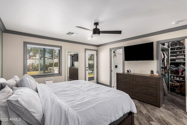 bedroom featuring wood finished floors, visible vents, ornamental molding, a walk in closet, and access to outside