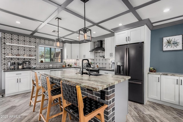 kitchen with visible vents, black refrigerator with ice dispenser, coffered ceiling, wall chimney exhaust hood, and a sink