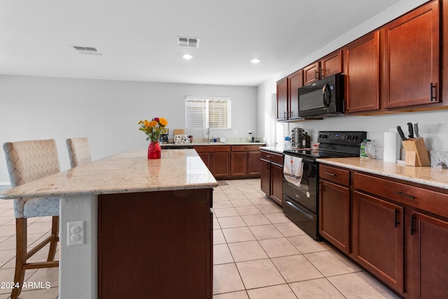 kitchen featuring light tile patterned flooring, black appliances, a kitchen breakfast bar, light stone countertops, and a kitchen island