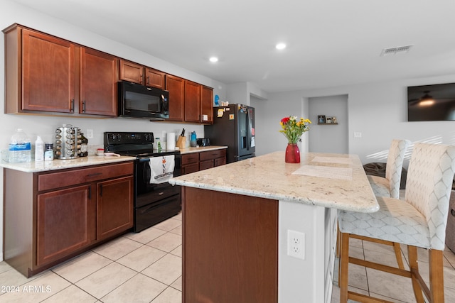 kitchen with a breakfast bar, a center island, black appliances, light tile patterned flooring, and light stone counters