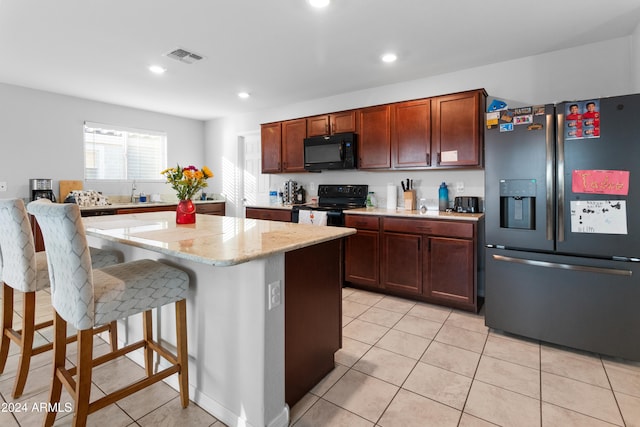 kitchen featuring light stone counters, light tile patterned flooring, black appliances, and a kitchen island