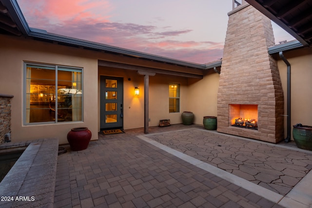 back house at dusk featuring a large fireplace and a patio area