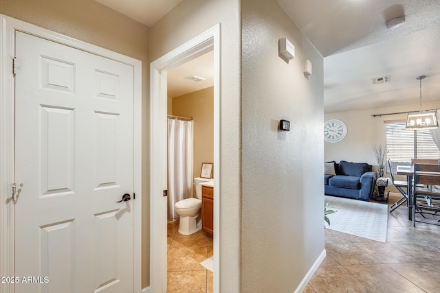 hallway with light tile patterned flooring and a notable chandelier