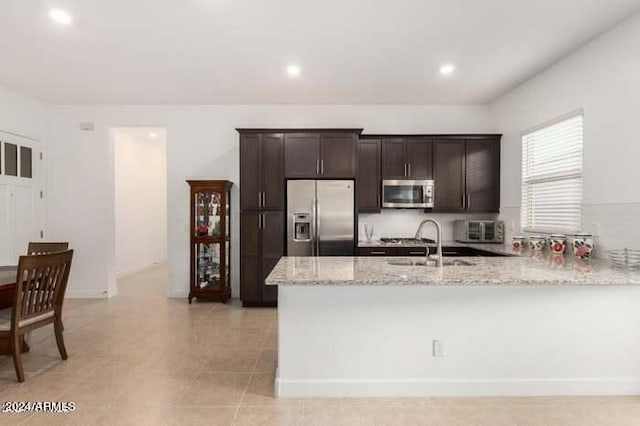 kitchen with dark brown cabinetry, light stone counters, sink, kitchen peninsula, and appliances with stainless steel finishes