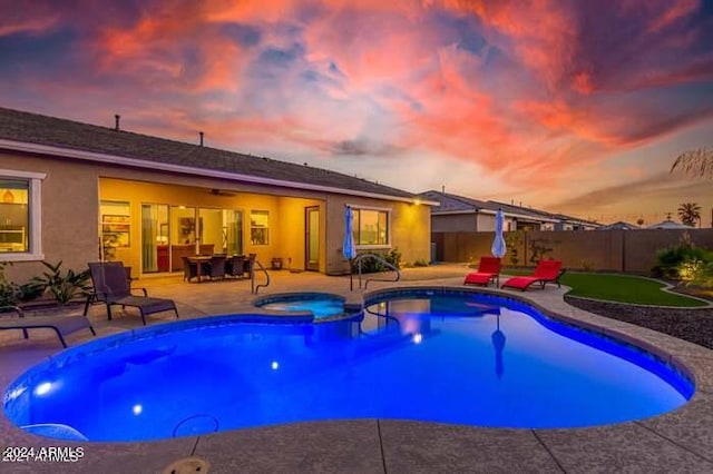 pool at dusk with an in ground hot tub and a patio