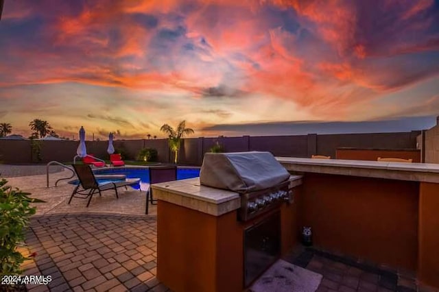 patio terrace at dusk featuring a fenced in pool and grilling area