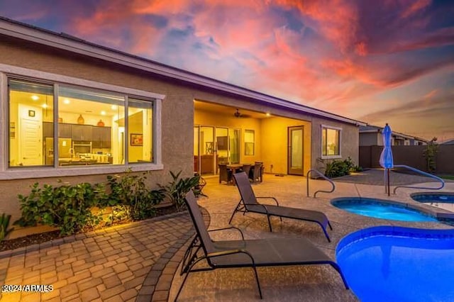 pool at dusk with an in ground hot tub and a patio area