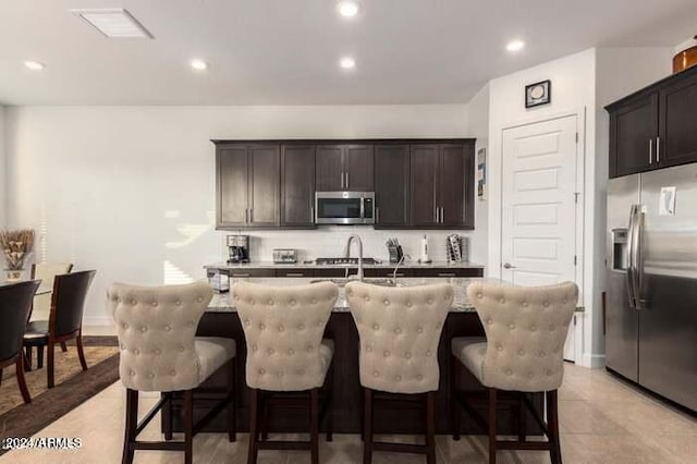 kitchen featuring dark brown cabinetry, a kitchen island with sink, appliances with stainless steel finishes, and a breakfast bar