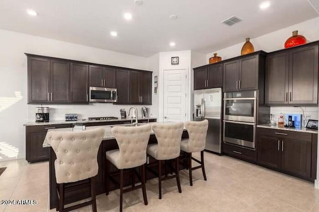 kitchen with an island with sink, dark brown cabinetry, a breakfast bar area, and stainless steel appliances