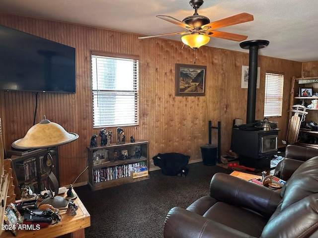 living area featuring wooden walls, baseboards, a ceiling fan, a wood stove, and carpet