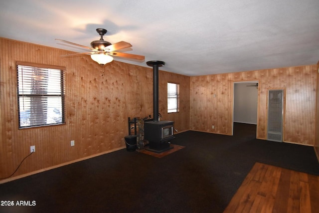 unfurnished living room with a ceiling fan, carpet, a wood stove, and baseboards