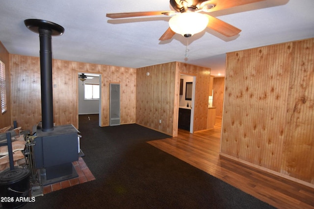 interior space with a wood stove, ceiling fan, wooden walls, and wood finished floors