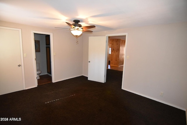 unfurnished bedroom featuring dark colored carpet, connected bathroom, baseboards, and ceiling fan