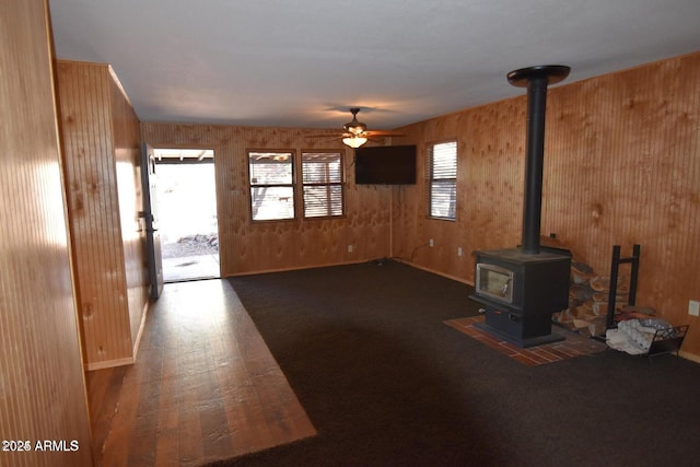 unfurnished living room with a ceiling fan, a wood stove, a healthy amount of sunlight, and wood finished floors