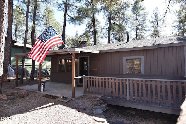 view of front of property featuring a patio, a chimney, and roof with shingles