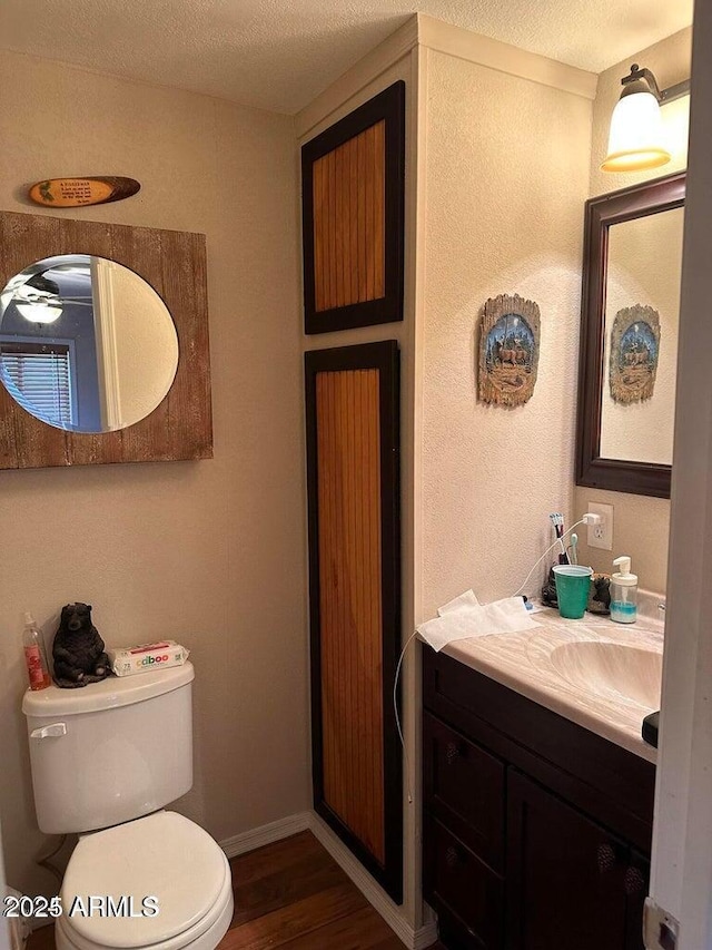 bathroom with toilet, vanity, a textured ceiling, wood finished floors, and baseboards