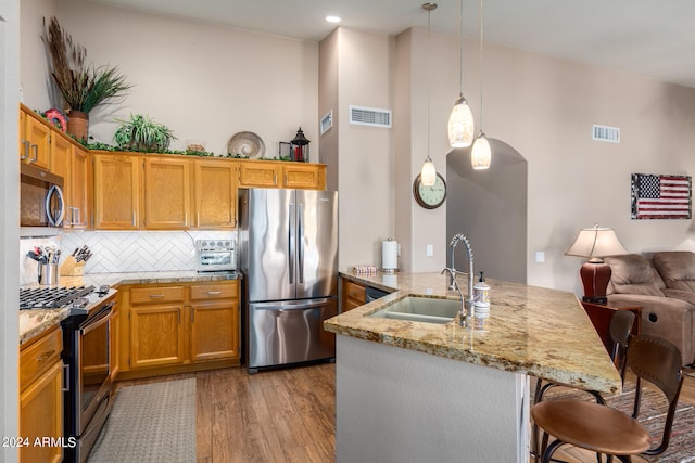 kitchen with pendant lighting, sink, hardwood / wood-style flooring, stainless steel appliances, and a breakfast bar area