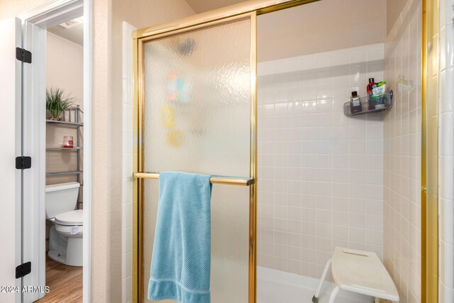 bathroom with hardwood / wood-style flooring, toilet, and a shower with shower door