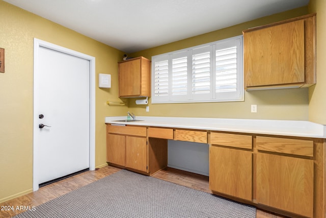 kitchen with light wood-type flooring, built in desk, and sink