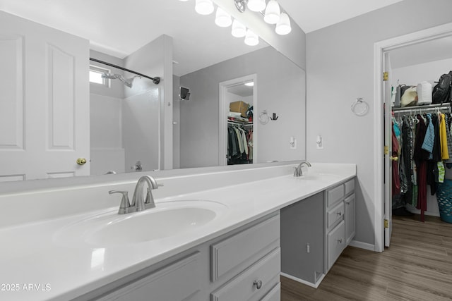 full bathroom featuring double vanity, walk in shower, wood finished floors, and a sink