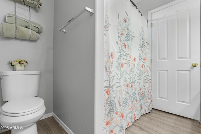 bathroom with toilet, a shower with shower curtain, baseboards, and wood finished floors