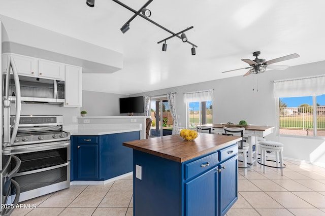 kitchen with butcher block counters, blue cabinets, light tile patterned flooring, and stainless steel appliances