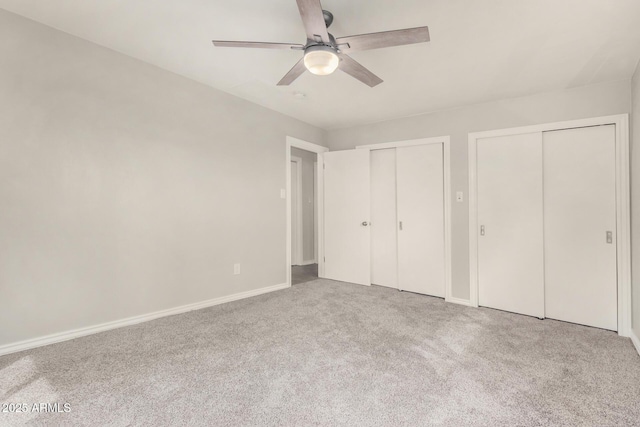 unfurnished bedroom with baseboards, multiple closets, carpet floors, and a ceiling fan