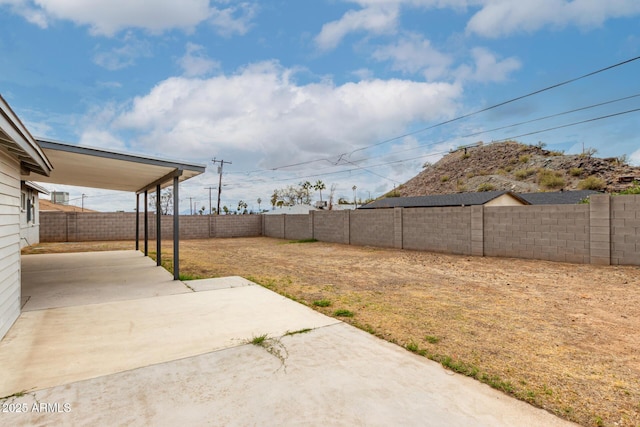 view of yard featuring an attached carport, a patio area, and a fenced backyard